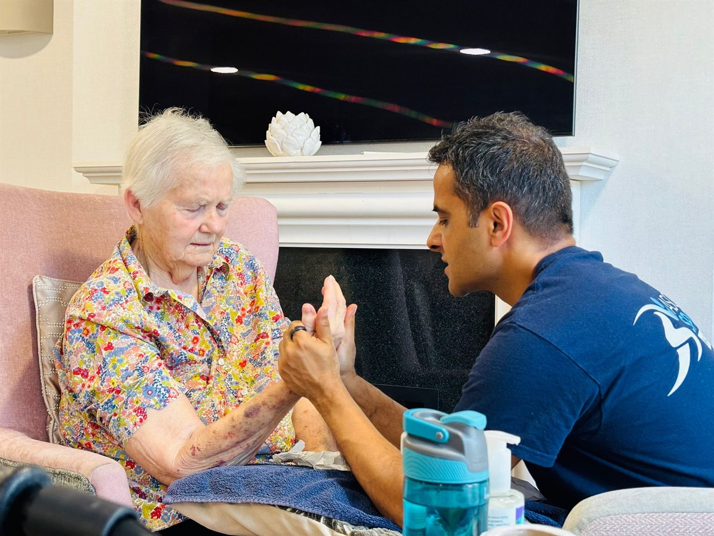 Pramod giving a gentle seated hand and arm massage to a care-home resident, fully clothed