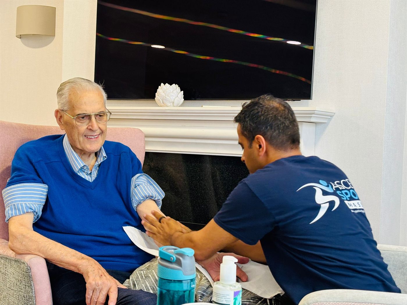 Pramod giving a gentle seated hand massage to a smiling care-home resident
